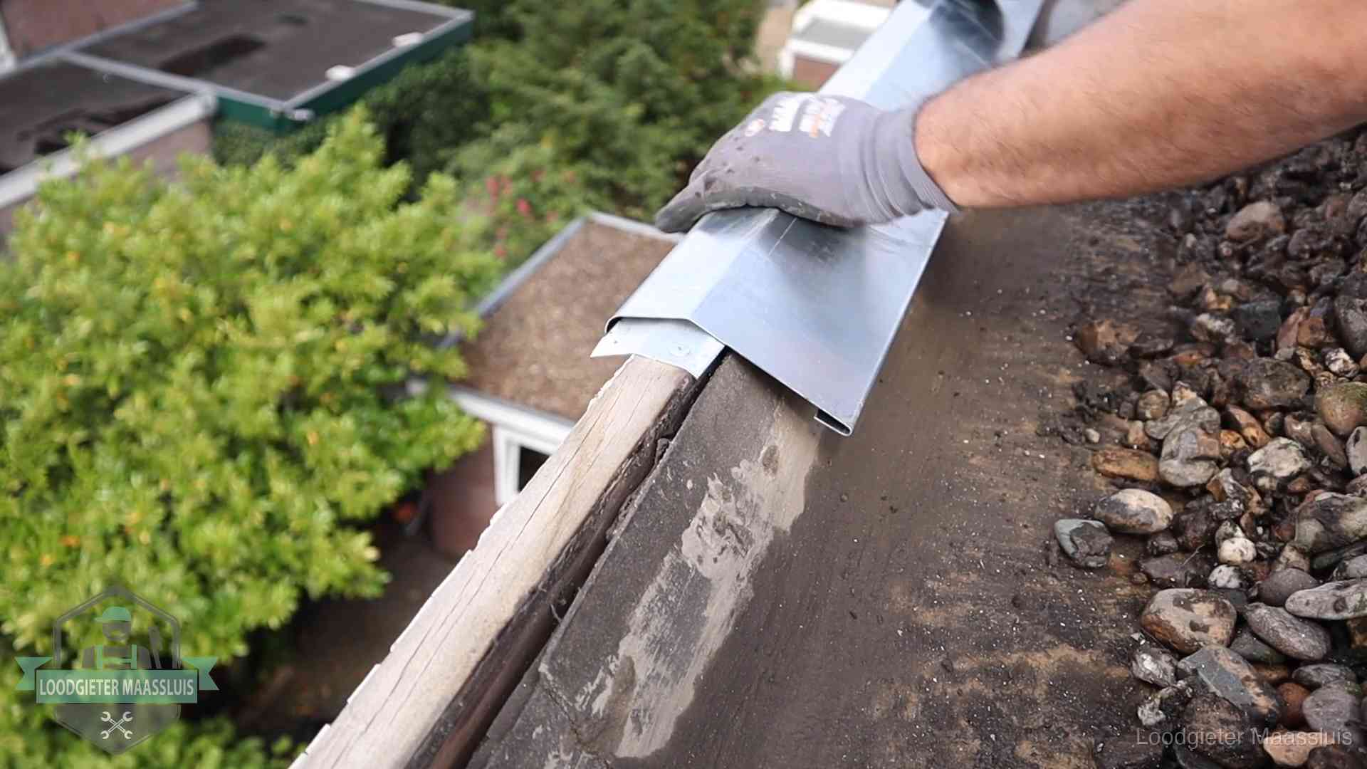 Daklekkage per wijk in Maassluis Dakdekker plaatst een zinken deklijst op een dakrand met uitzicht over een woonwijk in Maassluis