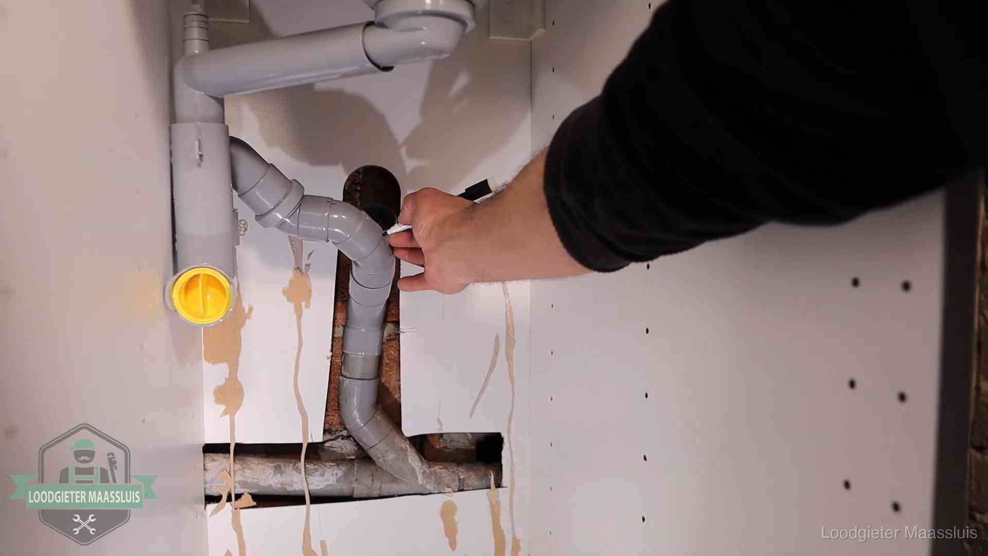 Loodgieter markeert een pvc-afvoerbuis onder een gootsteen in Maassluis