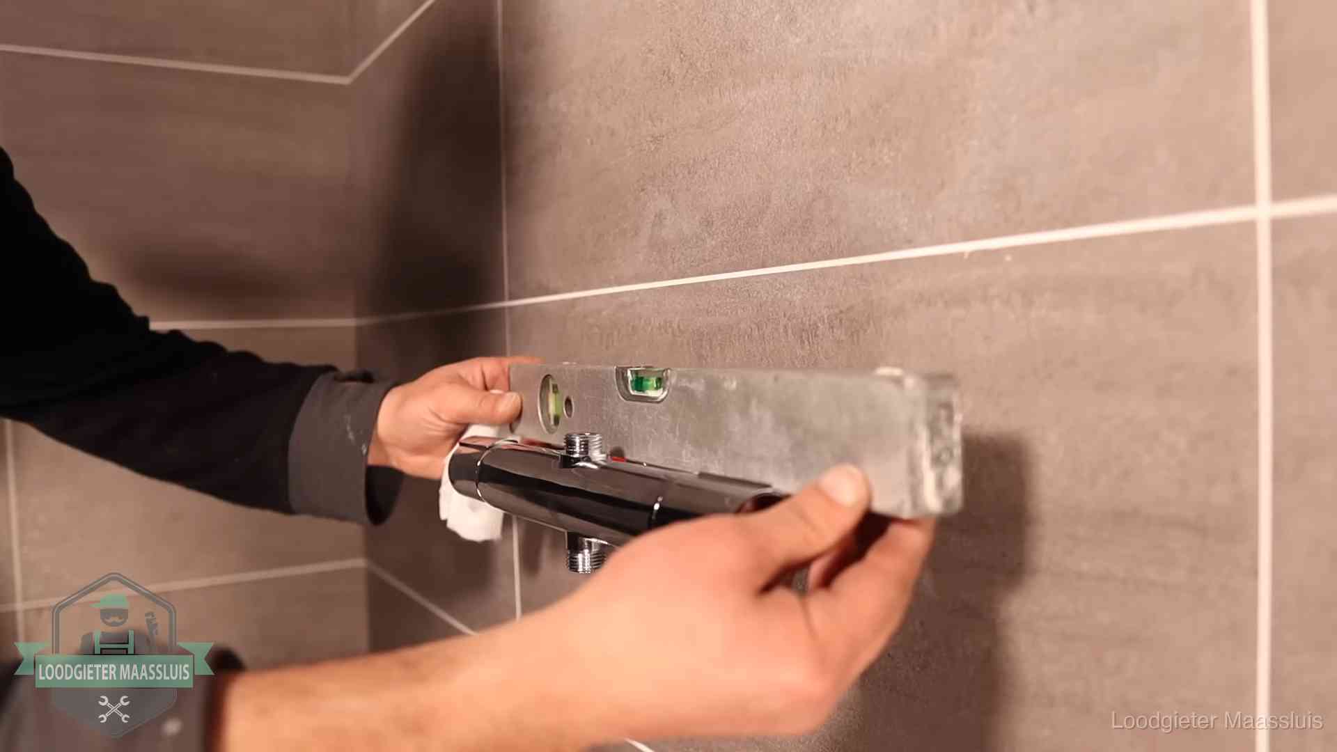 Loodgieter lijnt een douchekraan uit met een waterpas in een woning in Maassluis