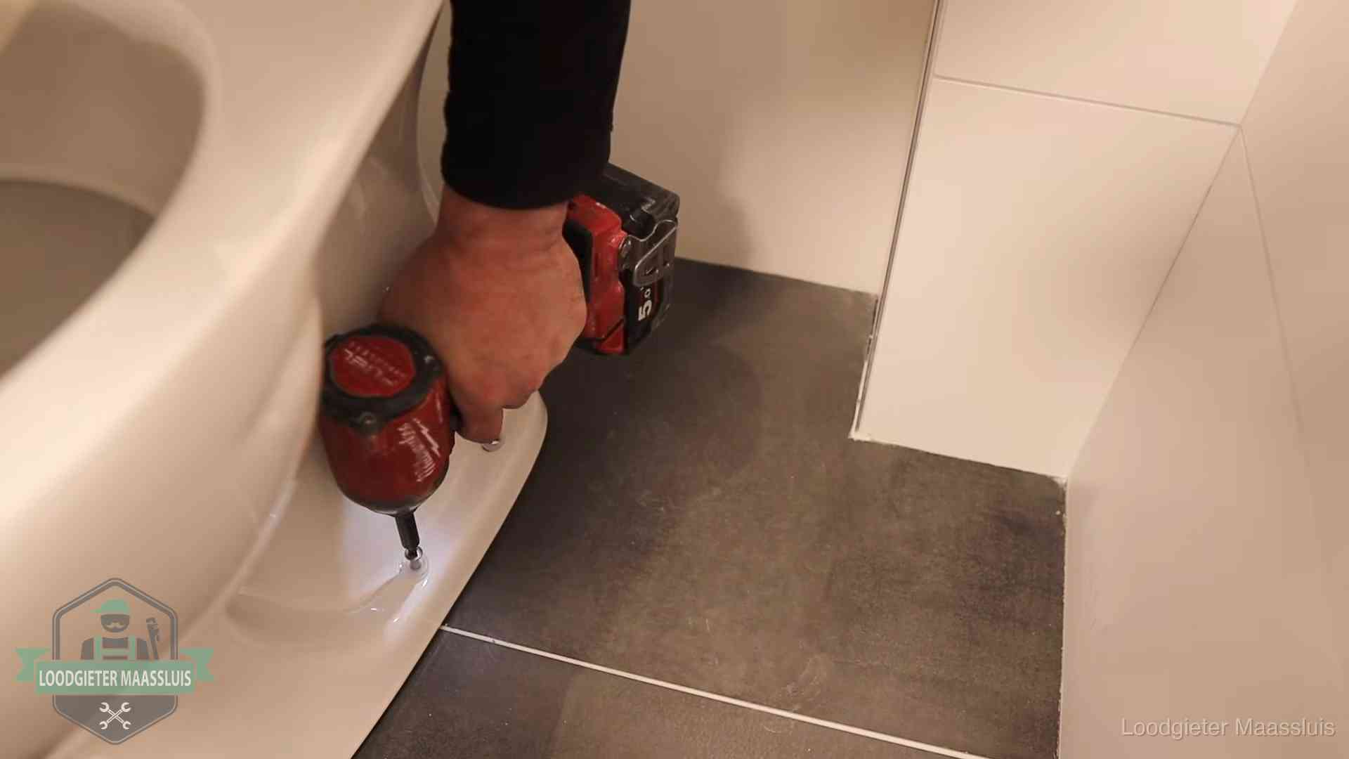 Loodgieter zet de voet van een wc-pot vast op de tegelvloer in Maassluis